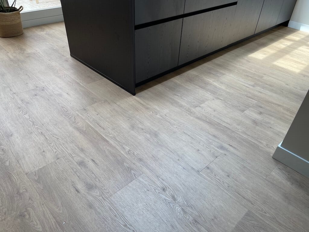 Lichte PVC-vloer in eikenlook bij een zwart keukeneiland