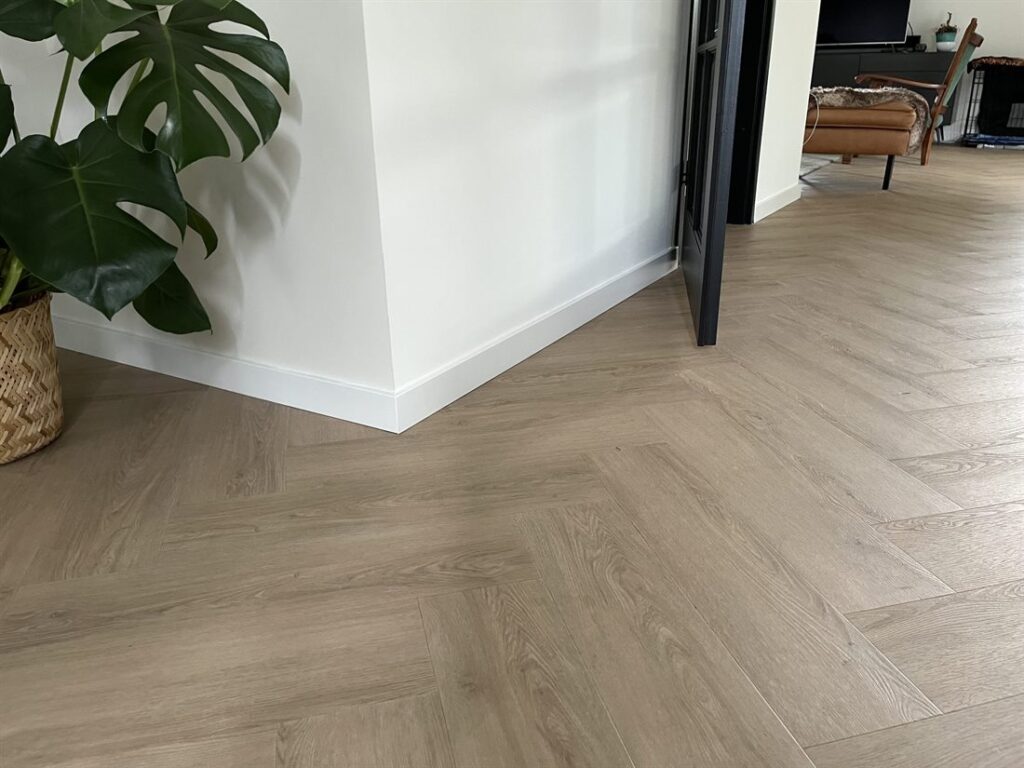 Visgraat PVC-vloer in warme eikenlook met witte plint en een plant