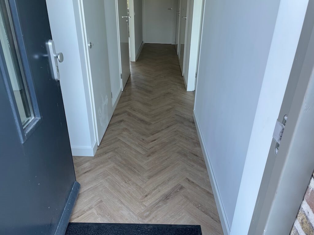 Visgraat PVC-vloer in een lange hal met witte deuren