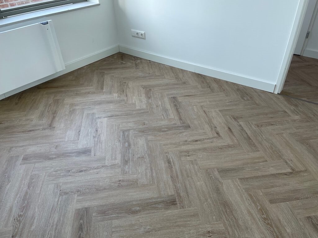 Visgraat PVC-vloer in grijsbruine eikenlook in een kamerhoek